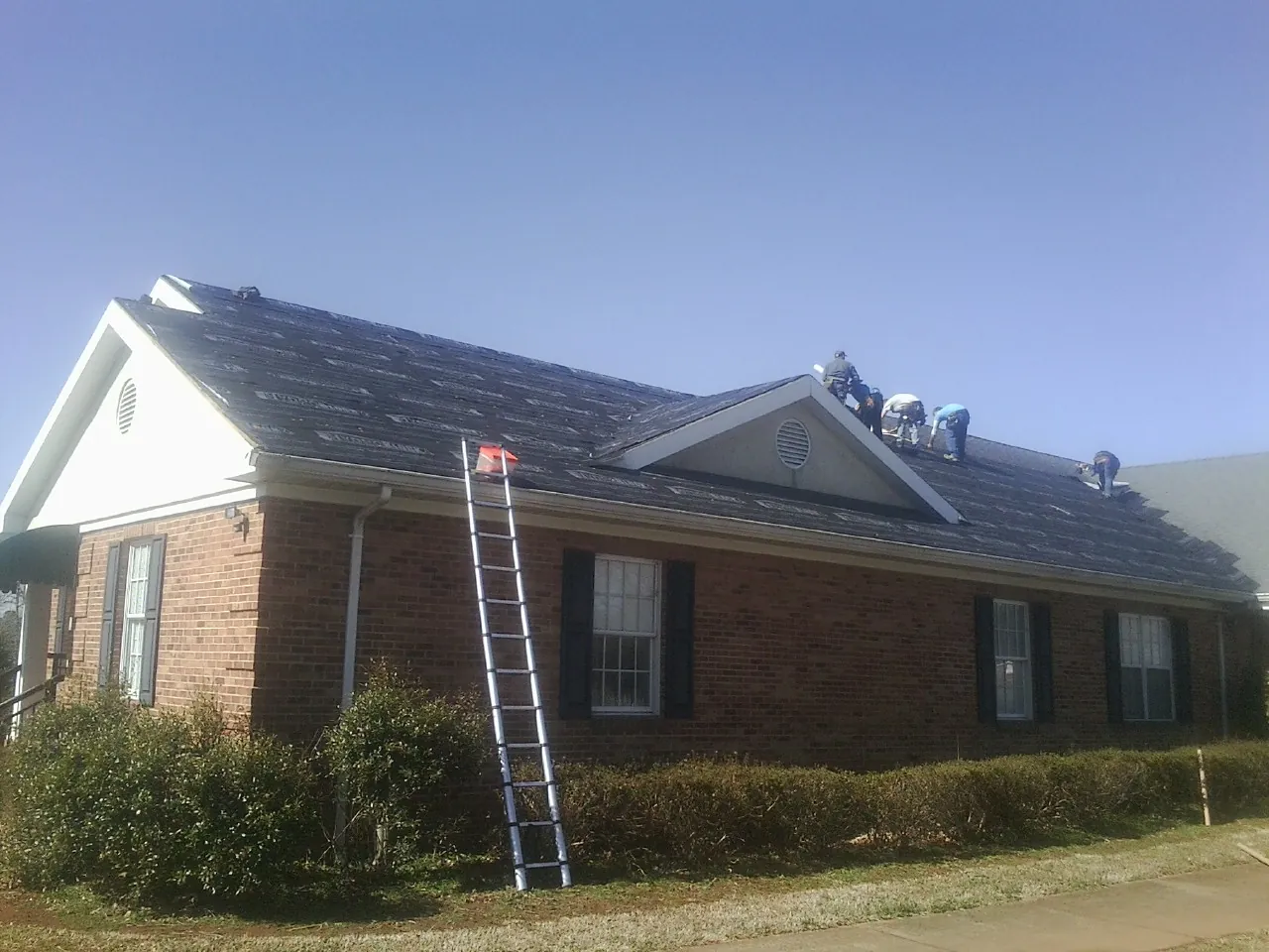 Crew tearing shingles off a brick ranch roof with a ladder set — Emergency Roof Repair work by our crew in Denville