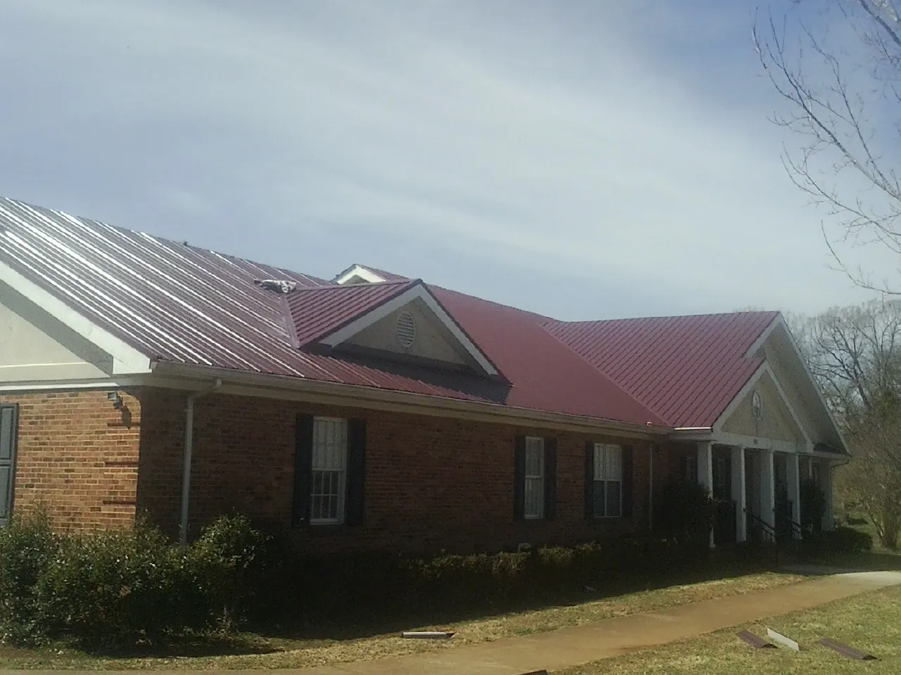 Red metal roof with gabled entries on a long brick building, from a Hail Damage Roof Repair job in Denville