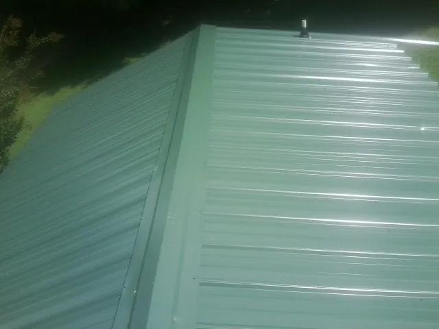 New green metal panels meeting at the ridge of a roof — Flat Roof Repair work by our crew in Denville