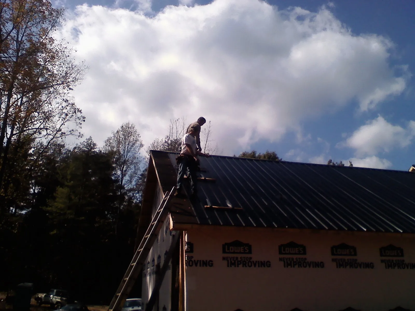 Roofer fastening dark metal panels high against a cloudy sky, from a Roof Inspection job in Denville