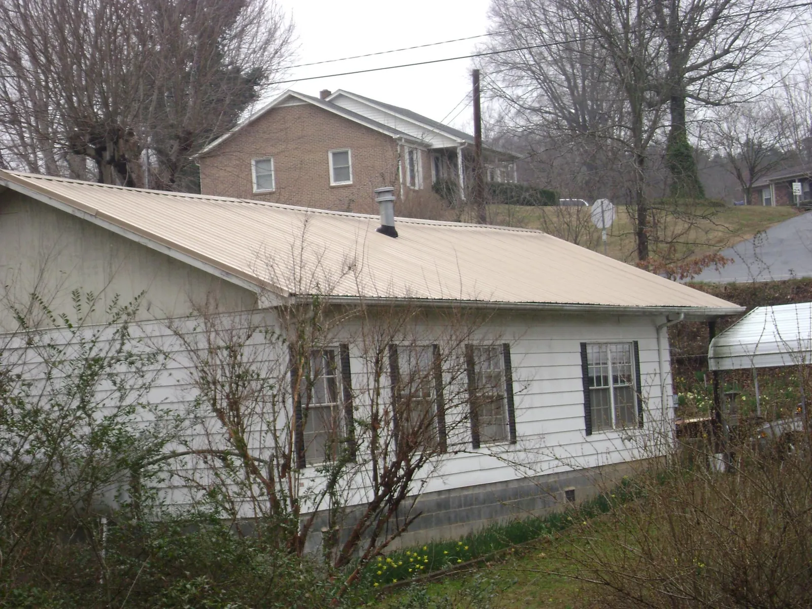 Tan metal roof on a white sided house set into a hillside — Commercial Roofing by Roofing Brothers in Denville